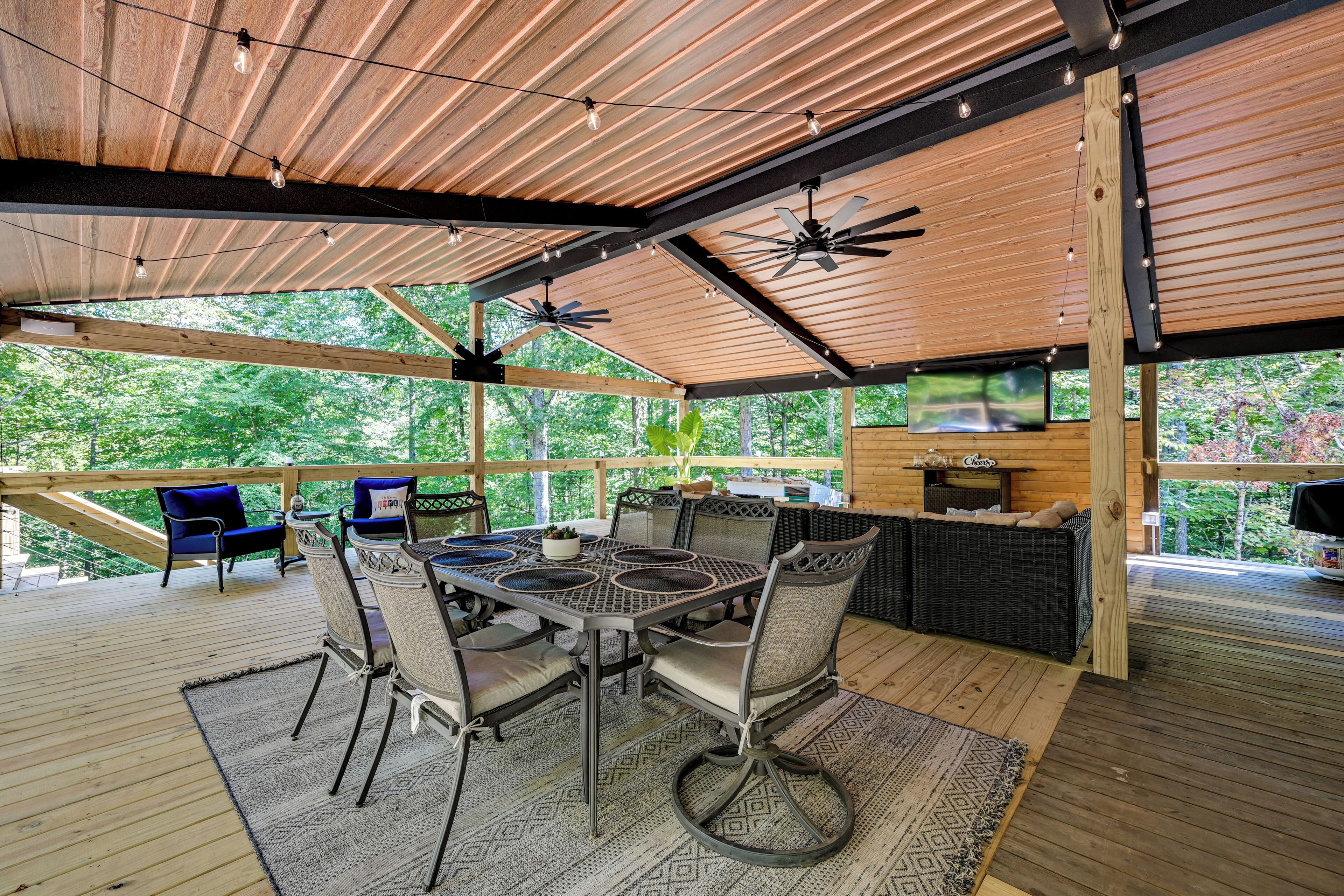 An outdoor patio with a table and chairs, a ceiling fan, and a TV screen.