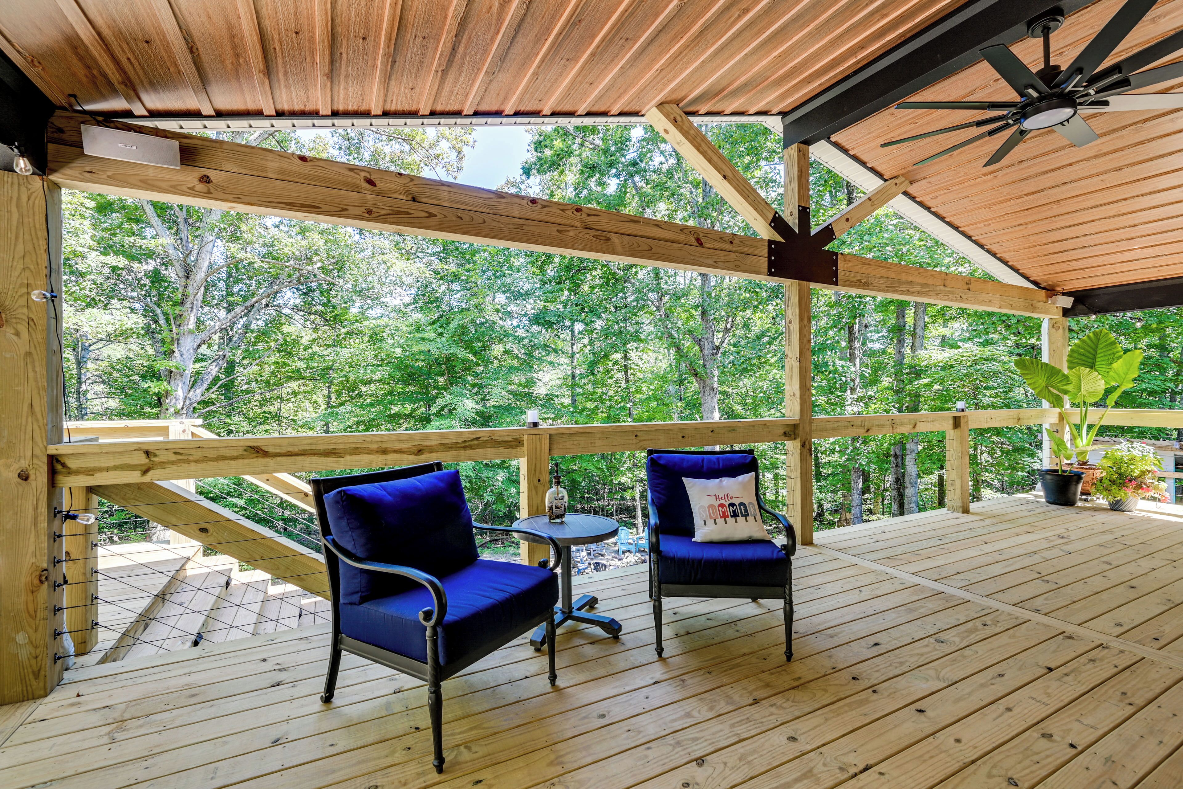 Una terraza de madera con dos sillas y una mesa, con vista a un área boscosa.