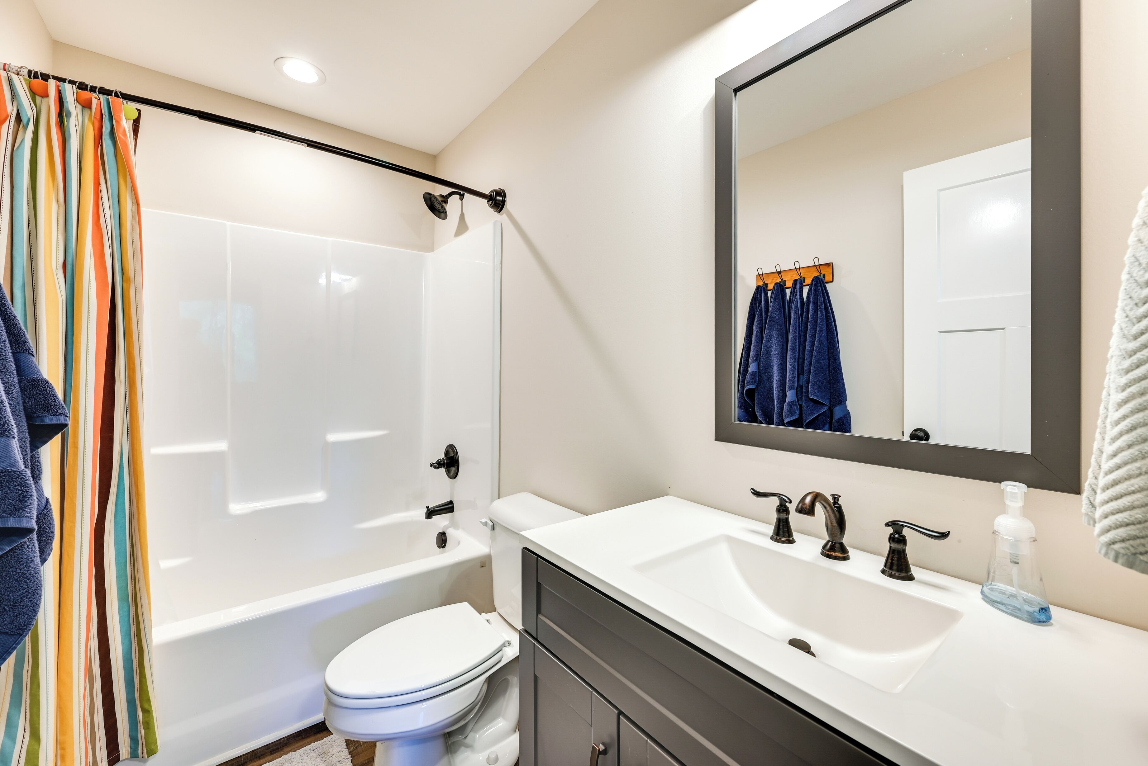A modern bathroom with a white bathtub, a white toilet, a large mirror, and a white sink with a soap dispenser.