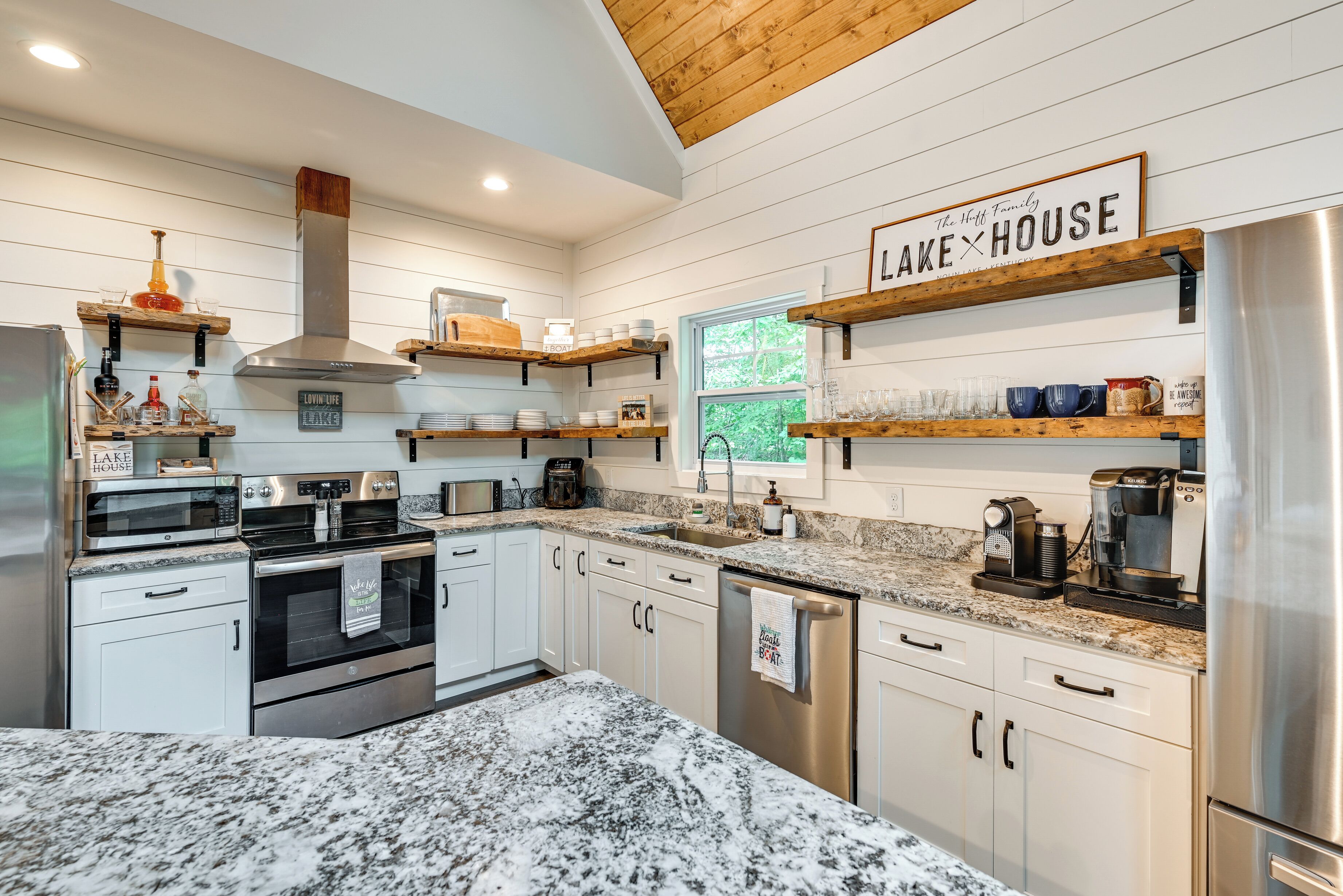 A modern kitchen with white cabinetry, granite countertops, and wooden shelves.