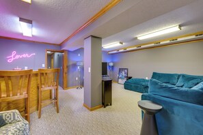 A modern living room with a teal sofa, wooden chairs, a neon sign, and a small table. - Hot Tub & Dock: Waterfront Bristol Area Retreat (Blountville)