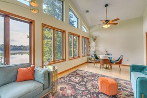 A spacious living room with a large window overlooking a lake, a ceiling fan, and a dining area with chairs and a table. - Hot Tub & Dock: Waterfront Bristol Area Retreat (Blountville)