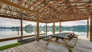 A wooden deck with picnic tables overlooking a calm lake, surrounded by a metal roof structure. - Waterfront Bristol Area Retreat w/ Boat Dock (Blountville)
