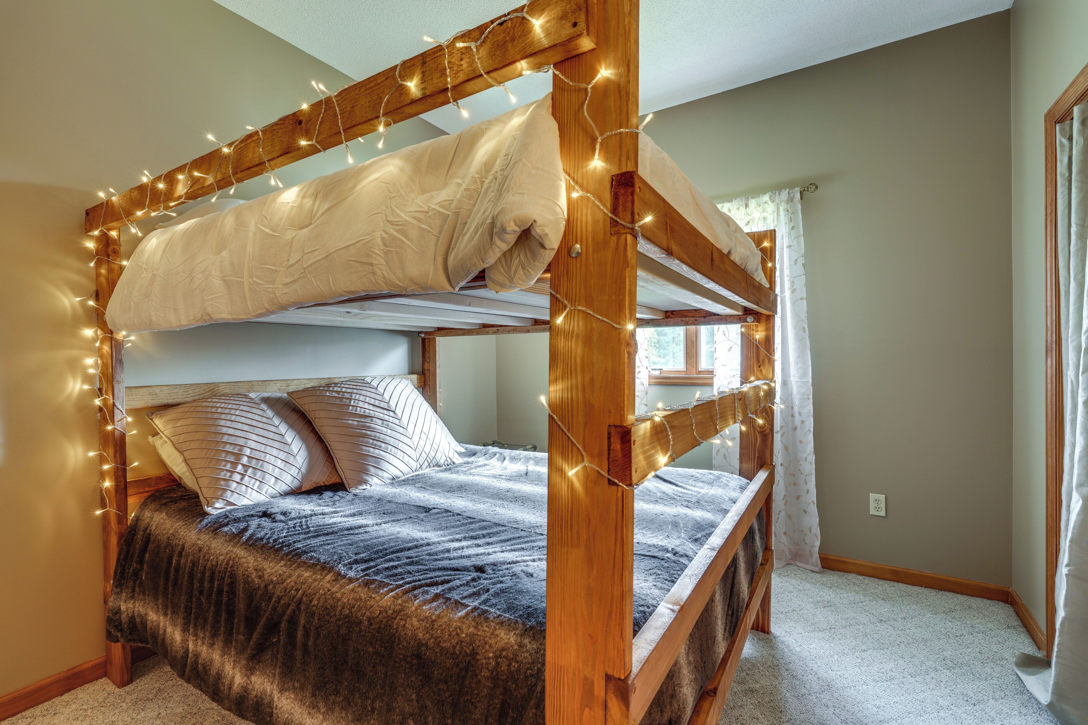 A bunk bed with a wooden frame, white bedding, and fairy lights.