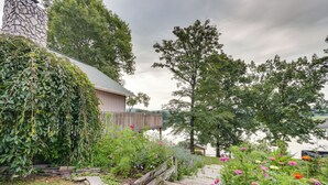 A house with a stone chimney, a wooden deck, and a garden with various plants and flowers. - Waterfront Bristol Area Retreat w/ Boat Dock (Blountville)
