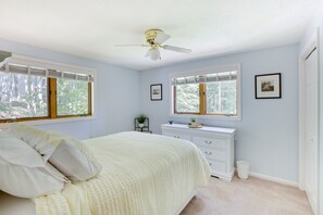 Ein Schlafzimmer mit einem Bett, einem Schminktisch, einem Deckenventilator und zwei Fenster mit Jalousien.