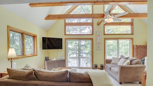 A cozy living room with a brown sofa, a beige couch, and a ceiling fan. There are large windows and a TV mounted on the wall. - Waterfront Lake Arrowhead Home w/ Dock! (North Waterboro)