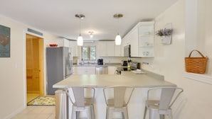 A modern kitchen with white cabinets, a central island with bar stools, pendant lighting, and a refrigerator. - Waterfront Lake Arrowhead Home w/ Dock! (North Waterboro)
