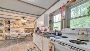 A kitchen with white cabinets, a stove, and a dining area with chairs. - Lakefront Michigan Abode w/ Deck & Fire Pit! (Cheboygan)