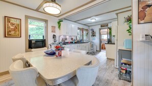 A modern kitchen with white cabinets, a large island, and a dining area with a white table and chairs. - Lakefront Michigan Abode w/ Deck & Fire Pit! (Cheboygan)