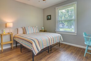 A bedroom with a bed, bedside tables, a lamp, a window with blinds, and a chair.