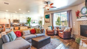 A modern living room with a sectional sofa, two armchairs, a fireplace, and a kitchen in the background.