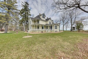 A large, two-story house with a wrap-around porch and a small deck, surrounded by a well-maintained lawn and trees. - Lake Michigan Vacation Rental w/ Private Beach! (Racine)