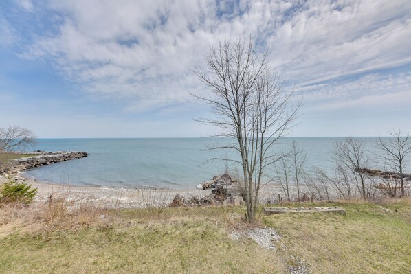 A coastal landscape with a clear sky, a rocky shoreline, and a leafless tree. - Lake Michigan Vacation Rental w/ Private Beach! (Racine)