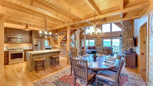 A spacious kitchen with wooden beams, a large island, and a dining area with a rug. - Hot Tub & Game Room: Spacious Nebo Cabin! (Nebo)