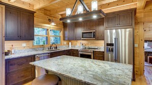 A modern kitchen with dark wood cabinets, granite countertops, stainless steel appliances, and a large island with stools. - Hot Tub & Game Room: Spacious Nebo Cabin! (Nebo)