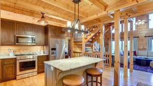 A spacious kitchen with wooden cabinets, a central island with stools, a microwave, and a refrigerator. - Hot Tub & Game Room: Spacious Nebo Cabin! (Nebo)