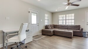 Un salon spacieux avec un canapé d’angle, un fauteuil de bureau blanc et un ventilateur de plafond.
