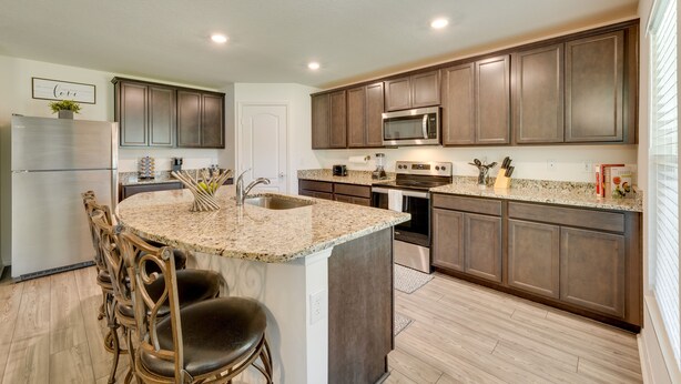 A modern kitchen with dark wood cabinets, a granite countertop, stainless steel appliances, and a central island with bar stools.