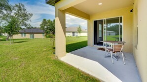 A covered patio area with a table and chairs, a clear view of the surrounding neighborhood, and a grassy lawn.