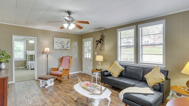 A living room with a wooden floor, a black leather sofa, a white coffee table, a red and white checkered chair, a small white table, and a ceiling fan.