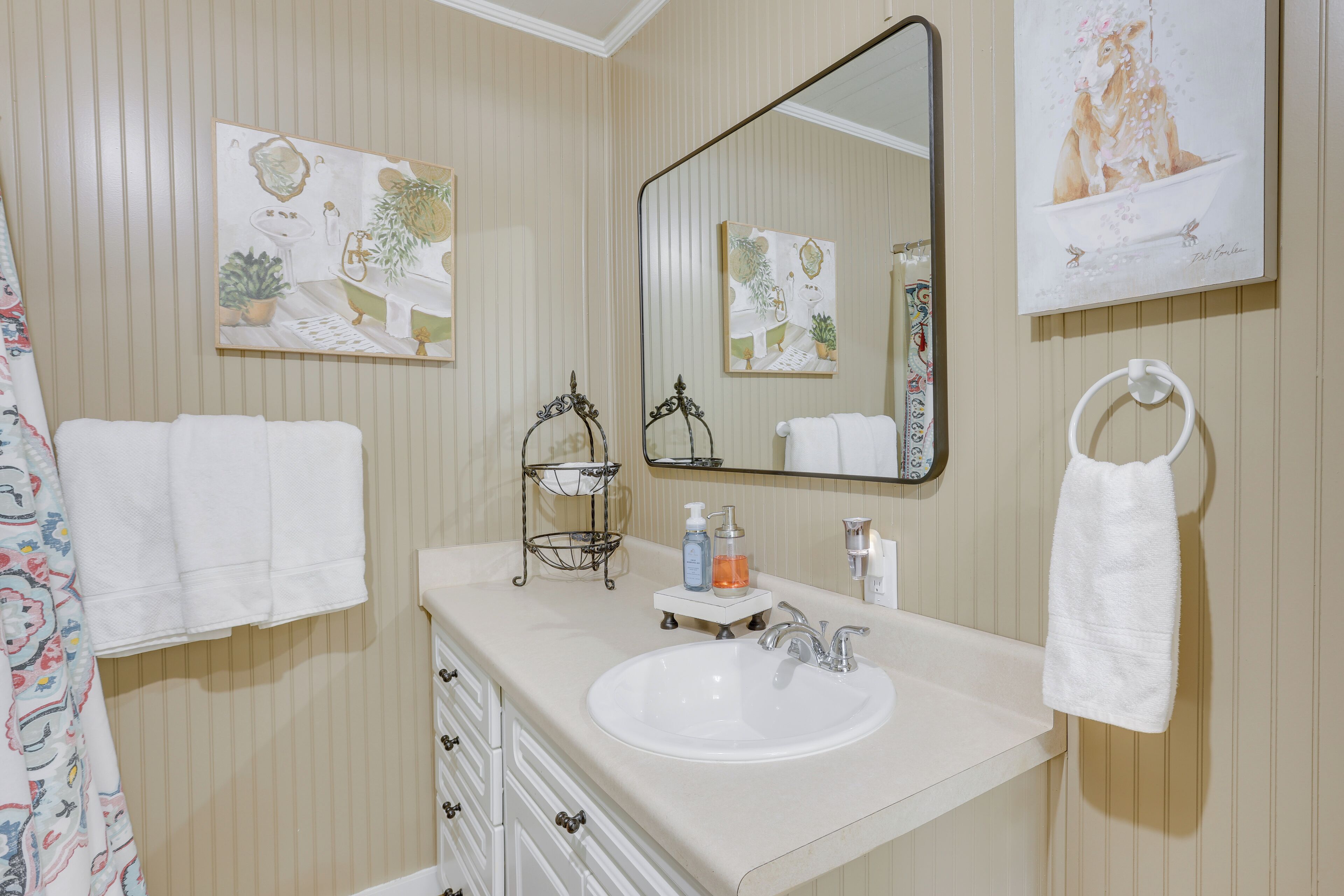 A bathroom with a sink, mirror, towel rack, and decorative wall art.