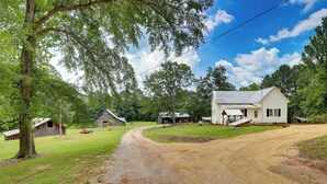 A rural property with a gravel driveway leading to a white house, surrounded by barns and lush greenery.