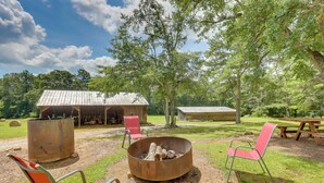 A rustic outdoor seating area with a metal fire pit, two red chairs, and a picnic table.