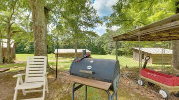Una terraza de madera con una parrilla, una silla blanca y un carrito rojo.