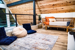 Un dormitorio acogedor con techo de madera, cama con ropa de cama naranja, sofá azul y alfombra estampada.