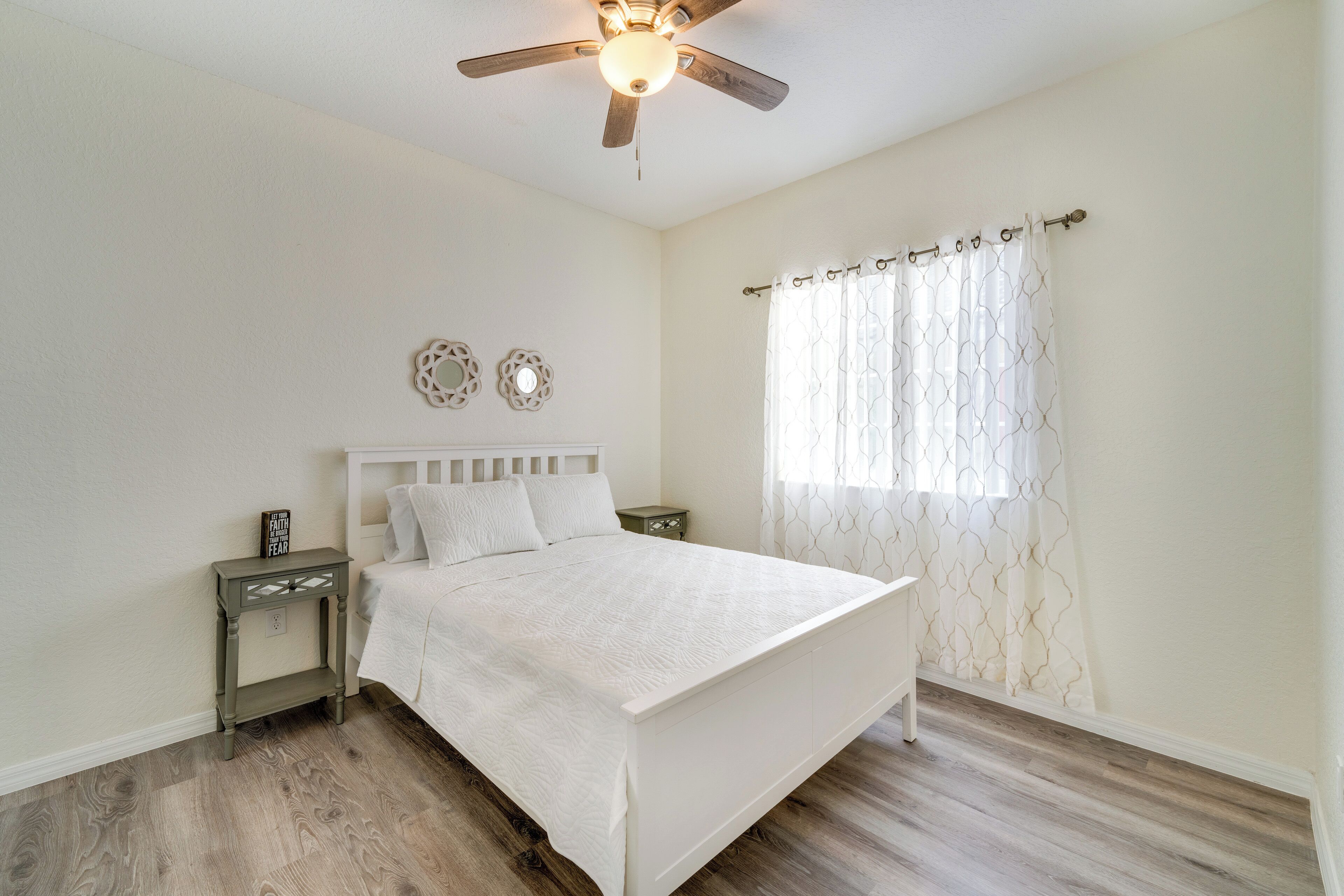 A bedroom with a bed, nightstand, ceiling fan, and decorative wall mirrors.