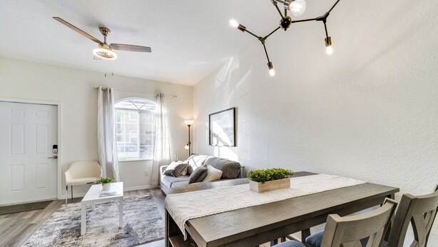 Un espace repas comprenant une table en bois, des chaises, un ventilateur de plafond et un lustre moderne.