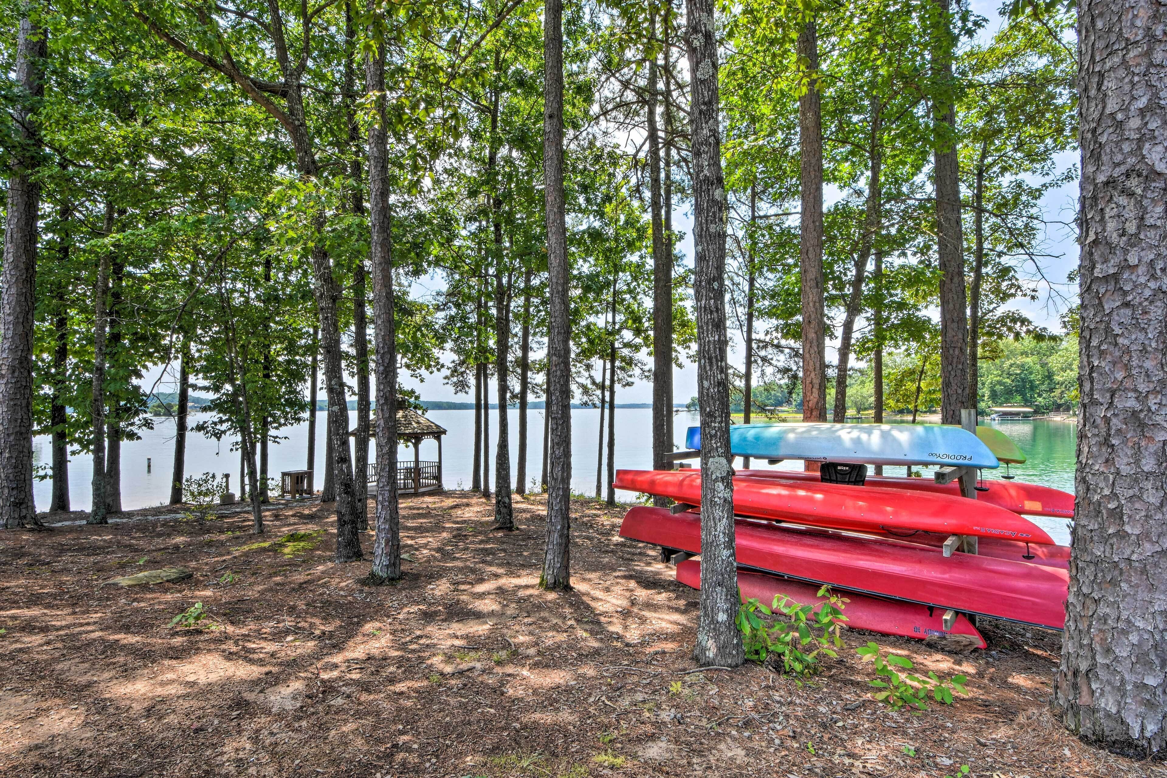 A serene lakeside setting with tall trees, a dock, and several red and blue canoes.