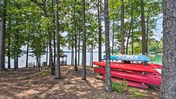 A serene lakeside setting with tall trees, a dock, and several red and blue canoes.