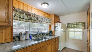 A kitchen with wooden cabinets, a granite countertop, a sink, a refrigerator, and a window with blinds. - Satsuma Home w/ Fire Pit + Dunns Creek Access! (Satsuma)