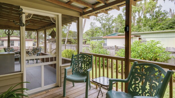 A covered outdoor patio with wooden flooring, two green chairs, a small table, and a potted plant. - Satsuma Home w/ Fire Pit + Dunns Creek Access! (Satsuma)