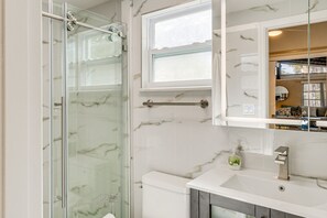 A bathroom with a glass shower enclosure, a white marble sink, and a mirror above the sink.