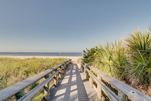 A wooden boardwalk leading to a beach with a clear sky.
