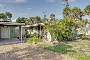 A single-story building with a covered porch, surrounded by palm trees and a gravel driveway.