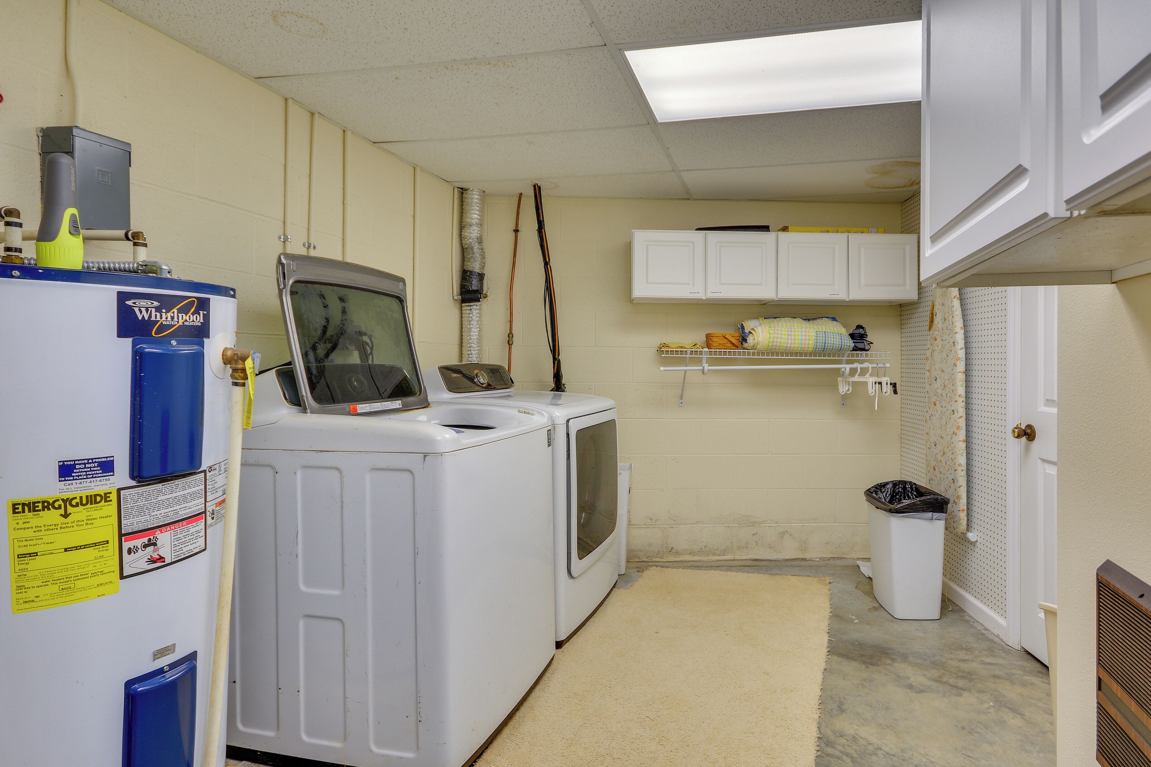 A laundry room with a Whirlpool washer and dryer, a trash can, and a shelf with laundry supplies.