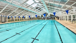 Piscina interior com pistas demarcadas, teto coberto e bandeiras azuis e brancas.