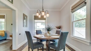 A dining area with a round wooden table, four upholstered chairs, a chandelier, and a window with blinds. - Cozy Tennessee Abode w/ Private Hot Tub & Fire Pit (Winchester)