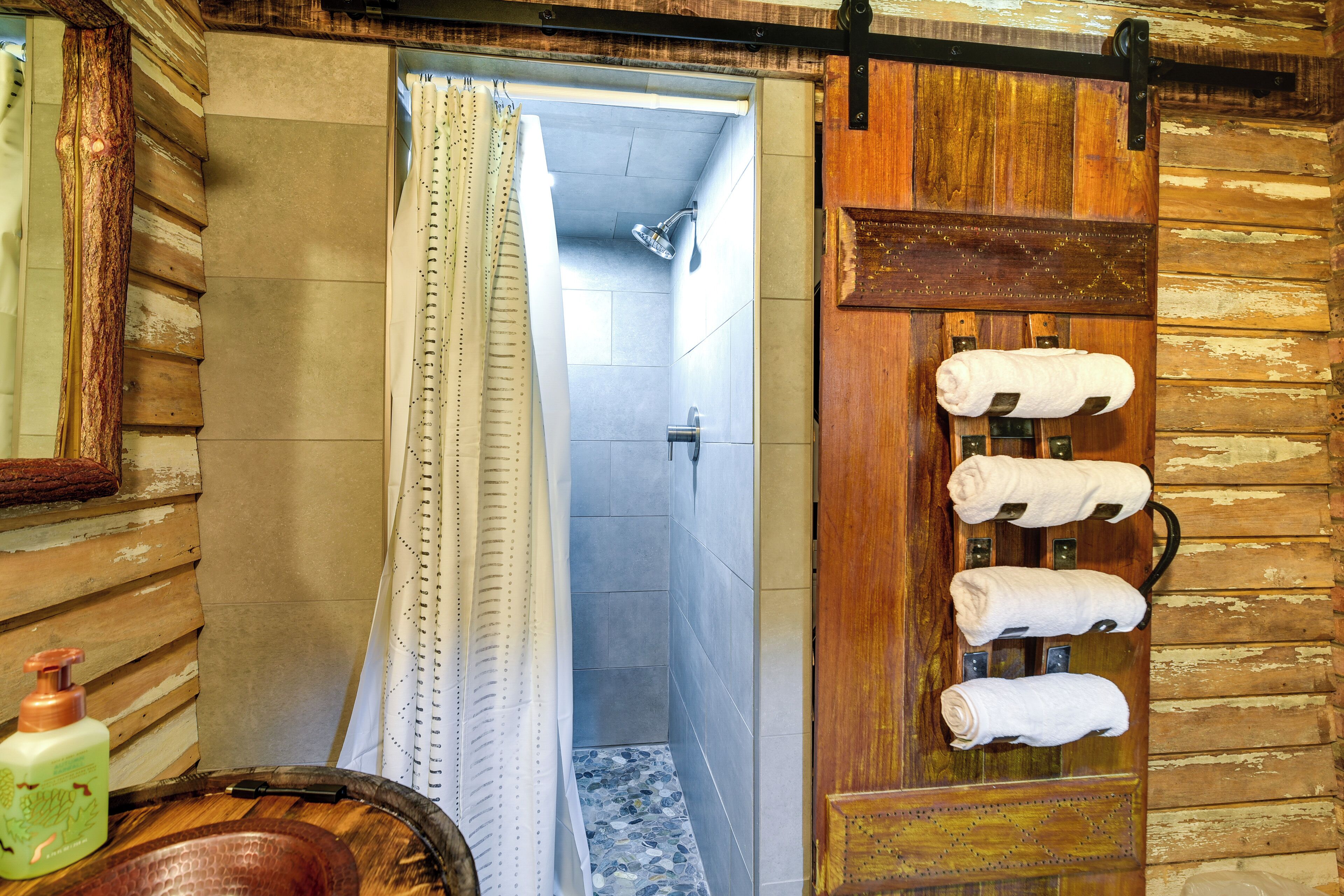 A rustic bathroom with a wooden door, a shower, and towels hanging on a rack.