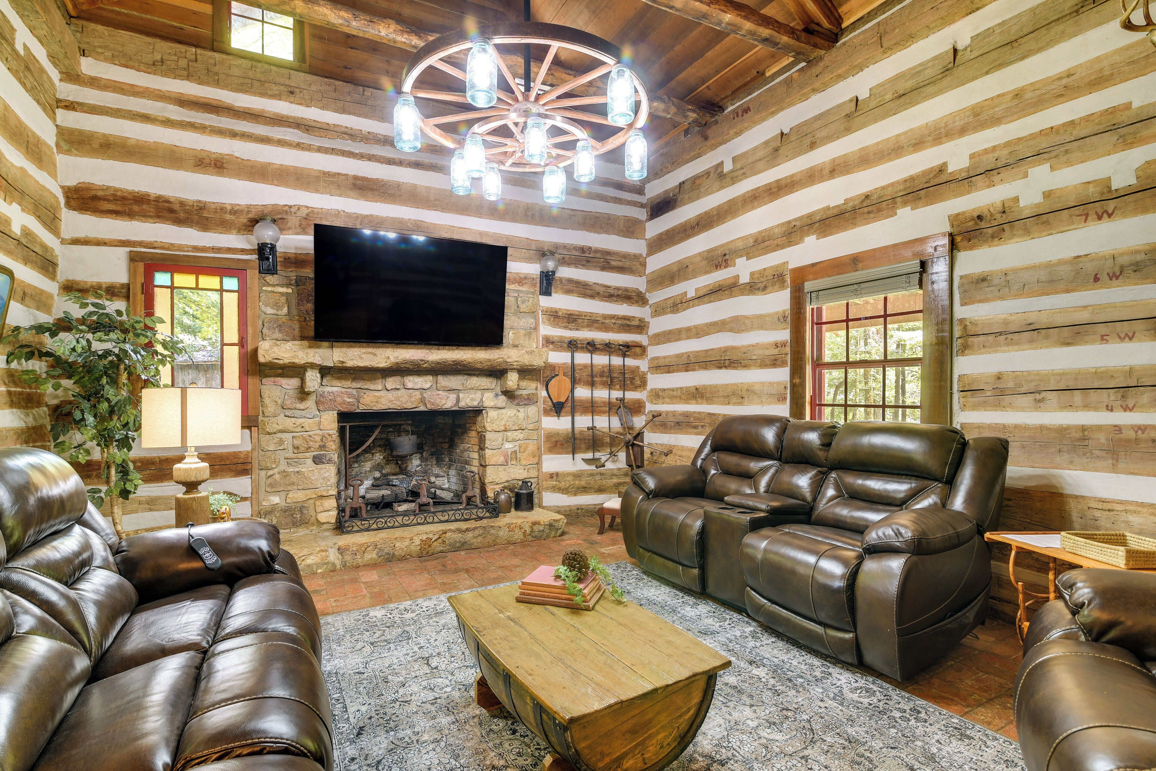A log cabin interior with a stone fireplace, leather sofas, and a mounted television.
