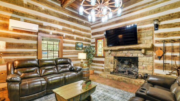 A log cabin interior with a leather sofa, a wooden coffee table, a stone fireplace, and a mounted television. - Glasgow Getaway w/ Patio, Fireplace & Grill! (Glasgow)
