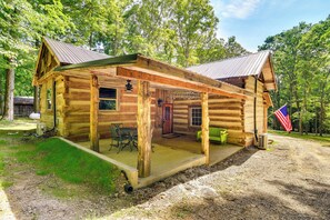 A rustic log cabin with a porch, a dining table, and a flag. - Glasgow Getaway w/ Patio, Fireplace & Grill! (Glasgow)