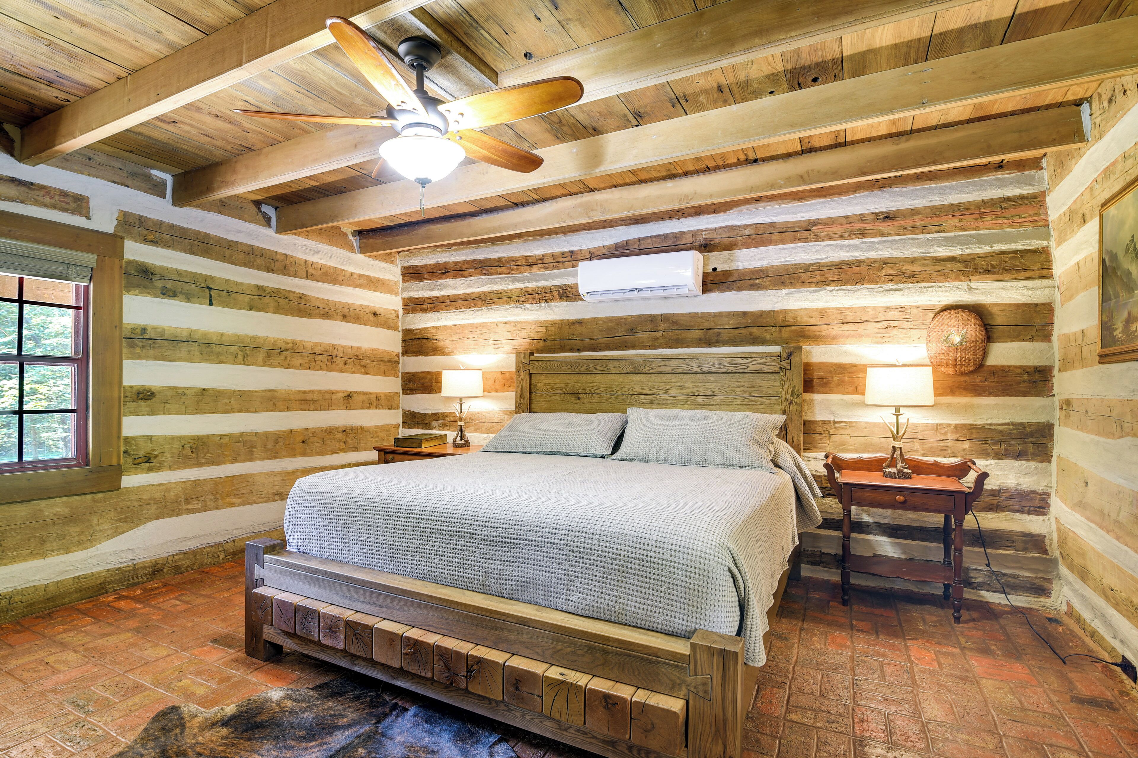 Une chambre située dans une cabane en rondins, avec un lit en bois, un ventilateur de plafond et une fenêtre.