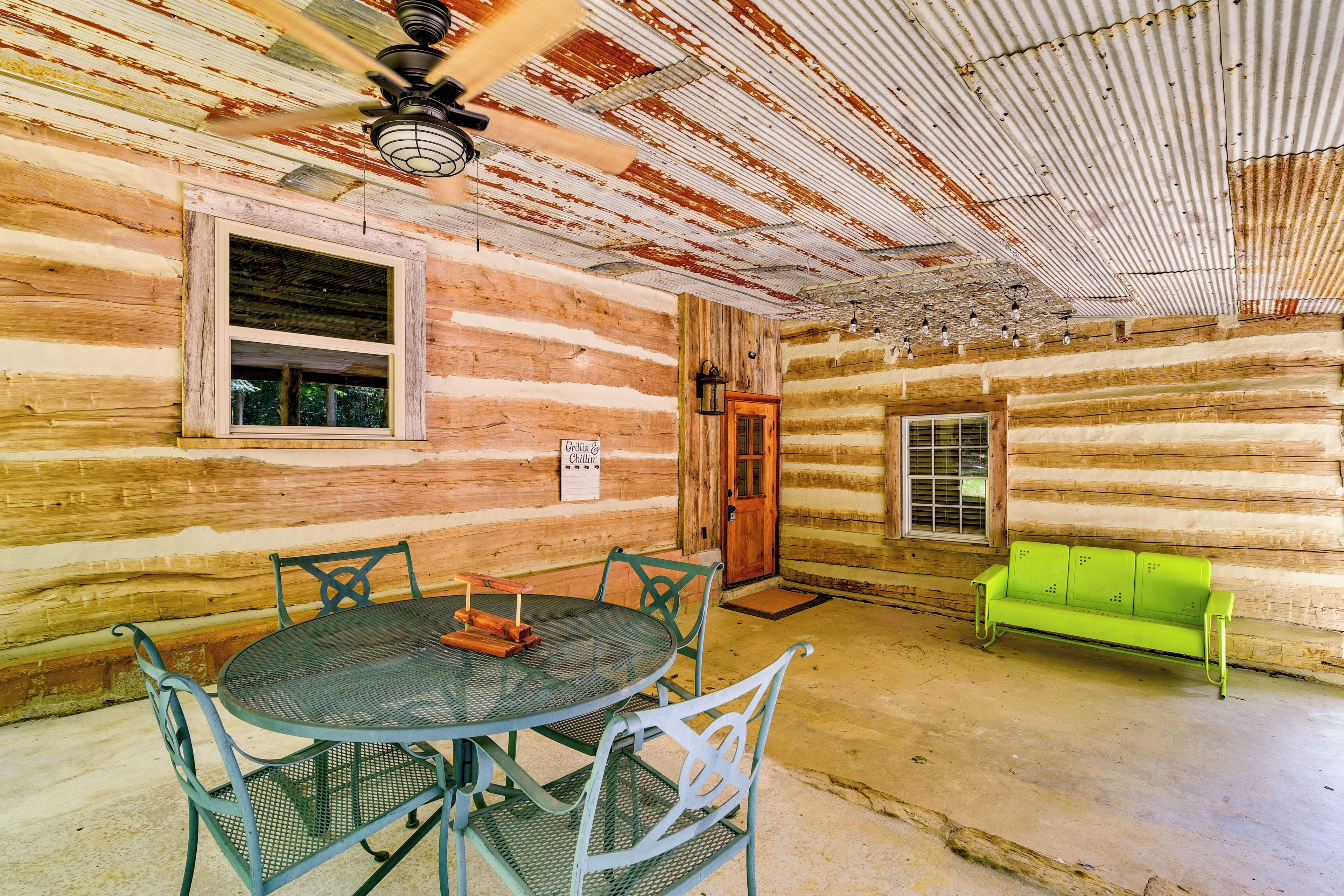 A rustic log cabin interior with a round metal table and chairs, a green bench, and a ceiling fan.