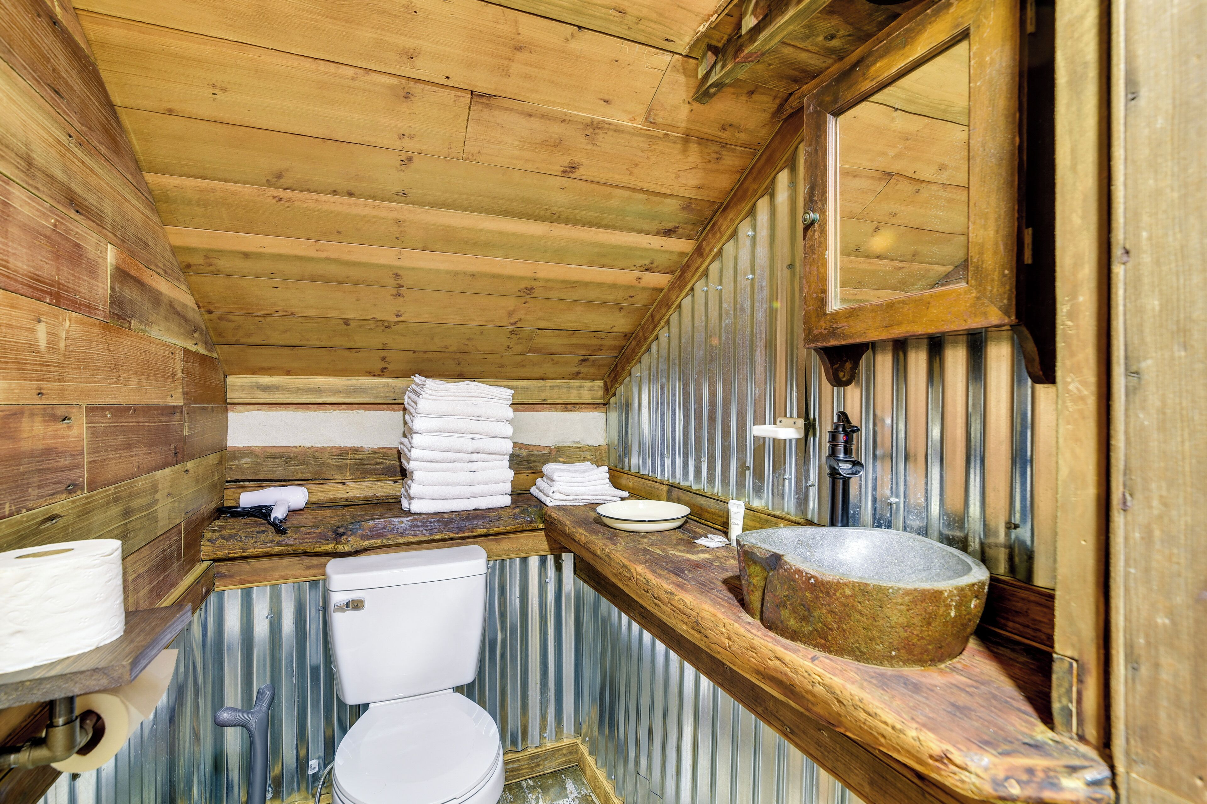 Ein rustikales Badezimmer aus Holz mit Toilette, Waschbecken und Spiegel.