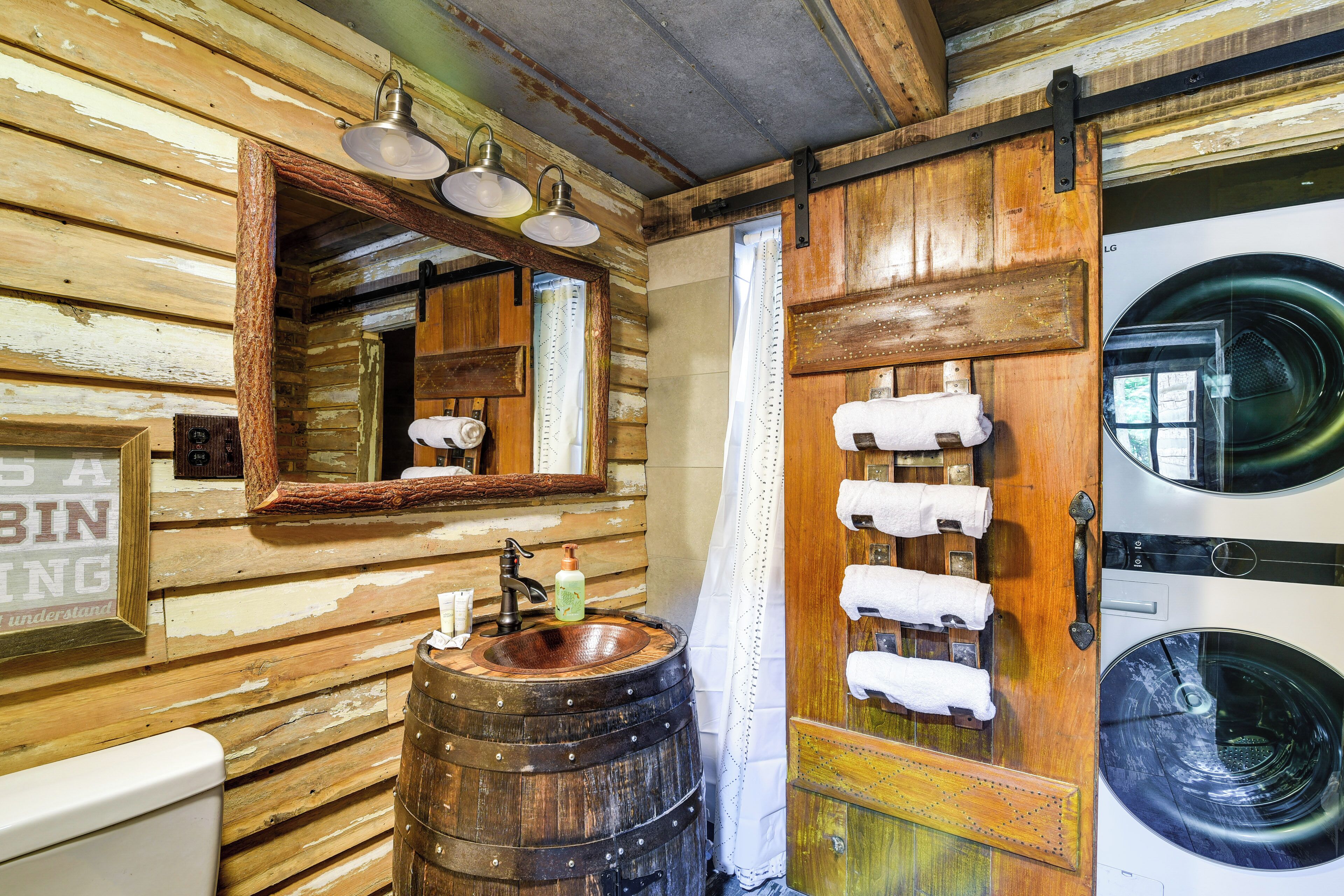 A rustic bathroom with a wooden barrel sink, a large mirror, and a washing machine.